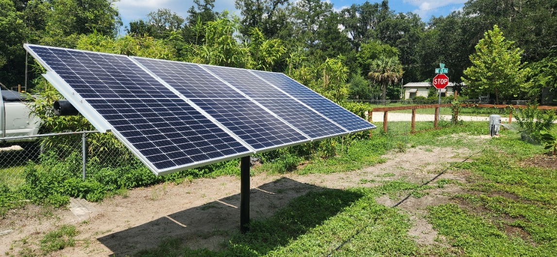 Solar panels installed in a green outdoor area, showcasing renewable energy solutions. A stop sign and residential elements are visible nearby.
