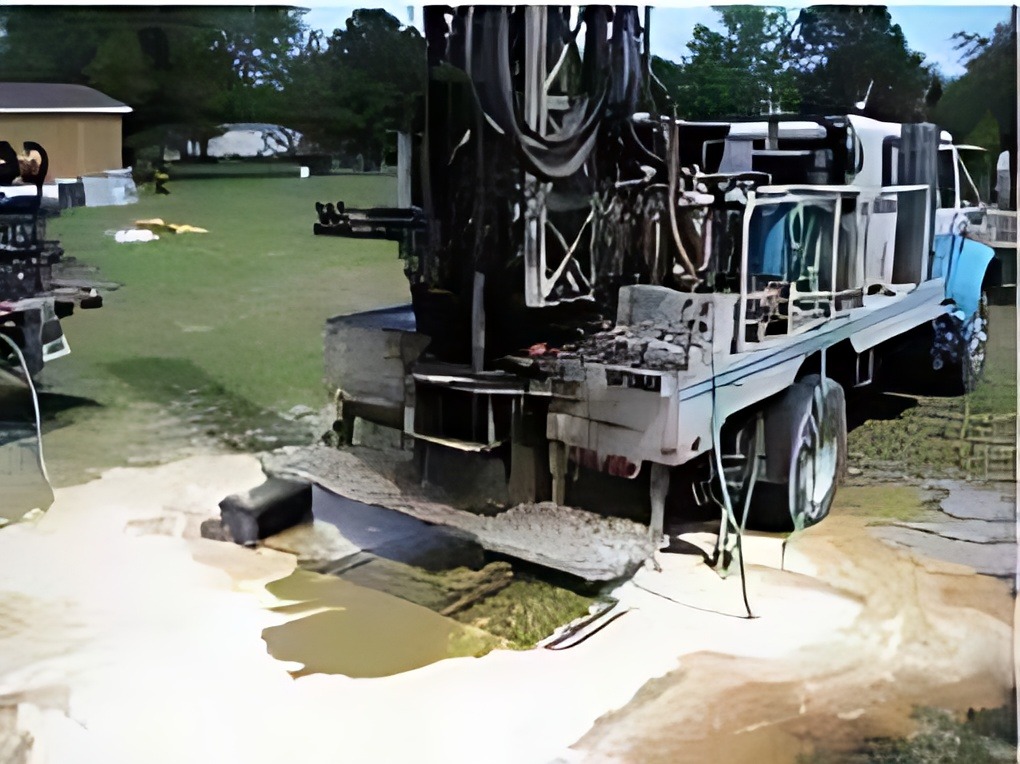 Large drilling truck positioned on grassy terrain, showing its equipment and machinery, indicating a site for drilling operations.